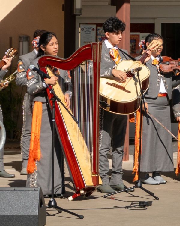 mariachi band playing outdoors: musicians holding guitars and a vihuela, dressed in traditional attire.