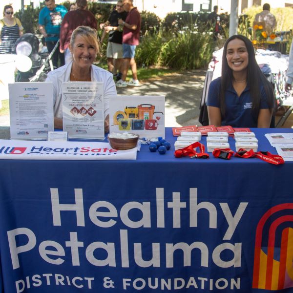 Two SRJC employees staffing a booth for Healthy Petaluma District & Foundation, promoting heart health with brochures and promotional items.