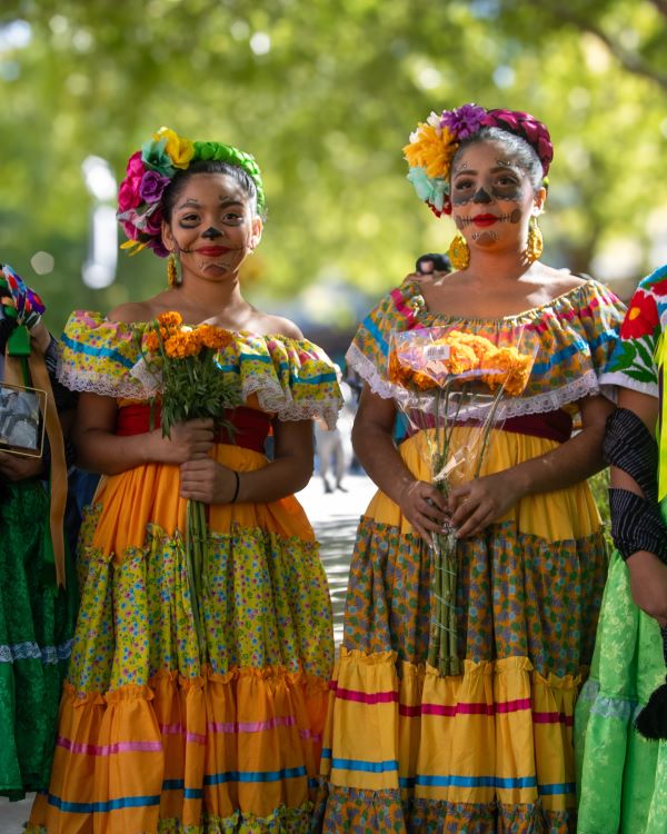 Two dancers in traditional Ballet Folklórico costumes—brightly colored long skirts and floral headpieces.