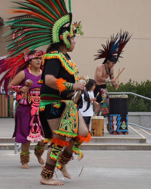 Three Aztec dancers in vibrant, traditional costumes.